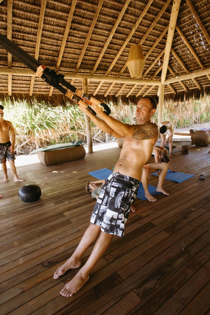 Adult men engaged in a lively outdoor crossfit session using resistance bands under a thatched roof.