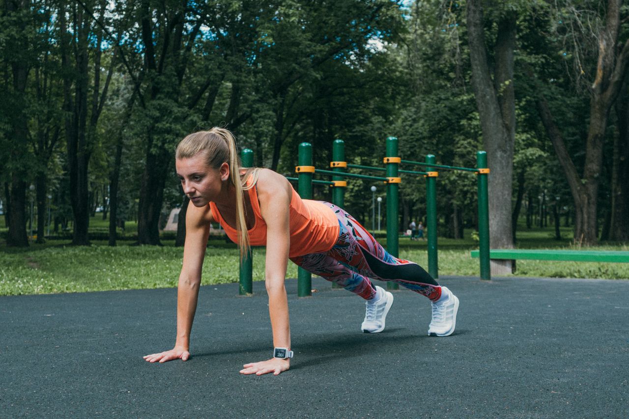 Woman performing push-up exercises outdoors in a park wearing active wear.